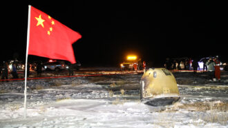 A capsule containing moon rocks next to a Chinese flag with vehicles in the background