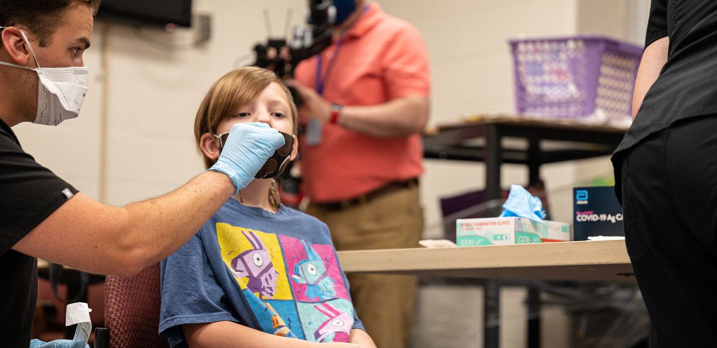 Elementary school student receiving a COVID-19 test from a person wearing a mask and gloves