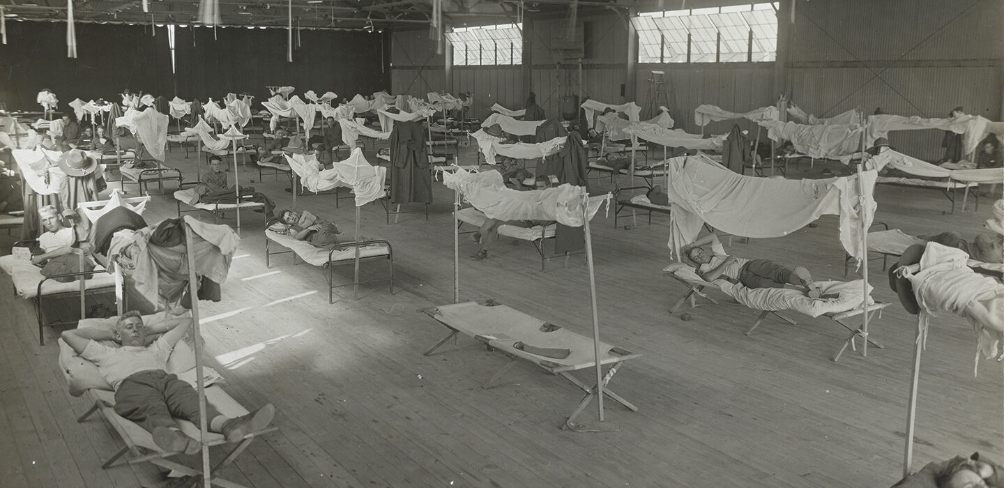 black and white photo of men on cots in an airplane hangar