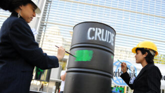 Two people painting an oil barrel green