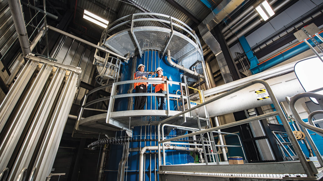 two researchers stand on a walkway in the FRIB's cryogenic plant