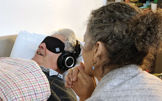 image of a patient lying on a couch wearing an eye mask and headphones while a therapist sits nearby