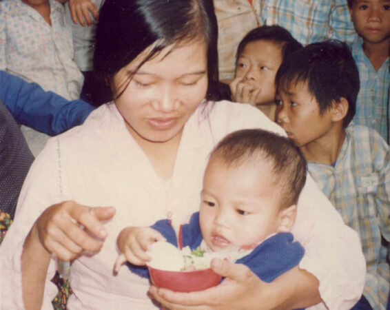 photo of a Vietnamese woman holding a baby eating rice out of a bowl