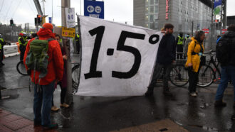 photo of a climate protester holding a sign that reads 1.5 degrees