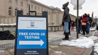 photo of a free covid testing sign and people standing in line to be tested