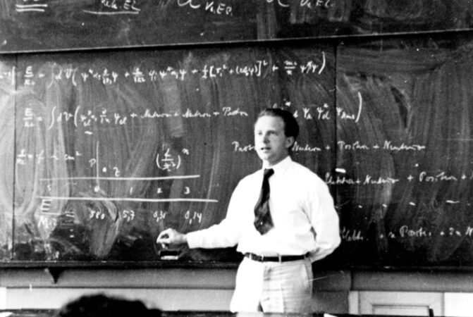 black and white image of Werner Heisenberg standing in front of a chalkboard