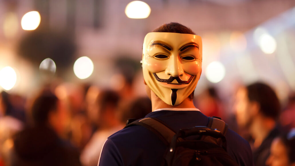 photo of a man in a crowd wearing a mask on the back of his head