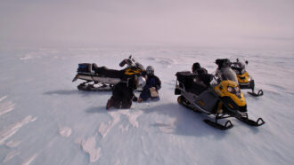 image of researchers crouched on the ice with snowmobiles