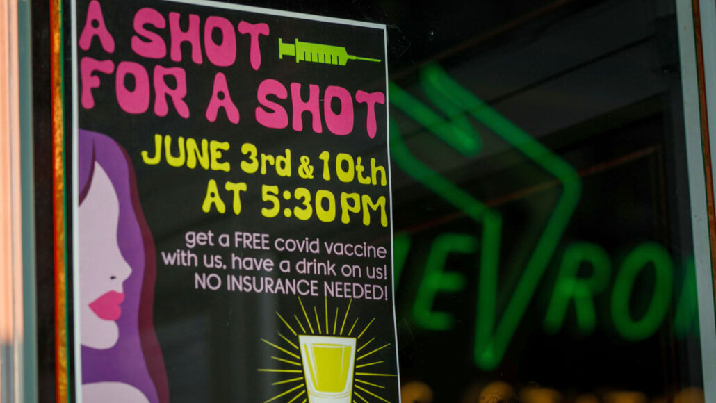 a sign outside a bar reading 'a shot for a shot' with a picture of a vaccine needle, advertising a free drink for people who got a COVID-19 vaccine