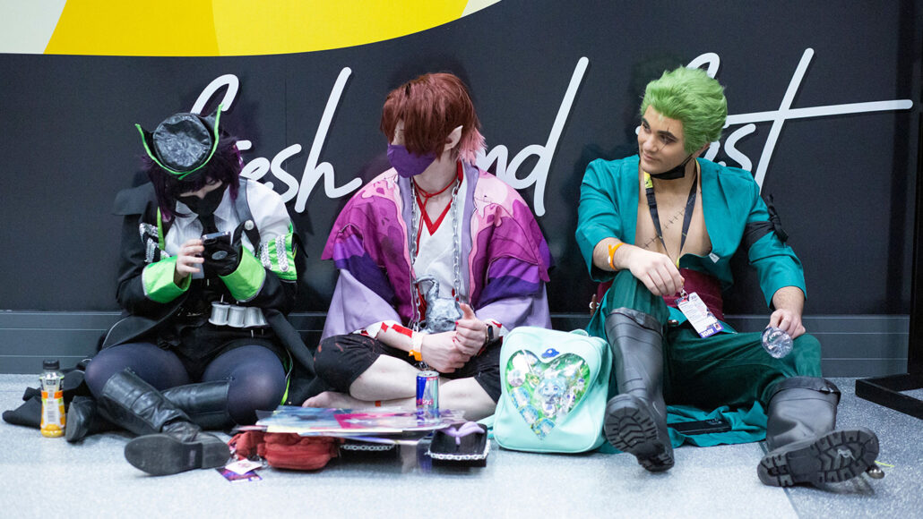 three people in costume sit against a wall at Anime NYC