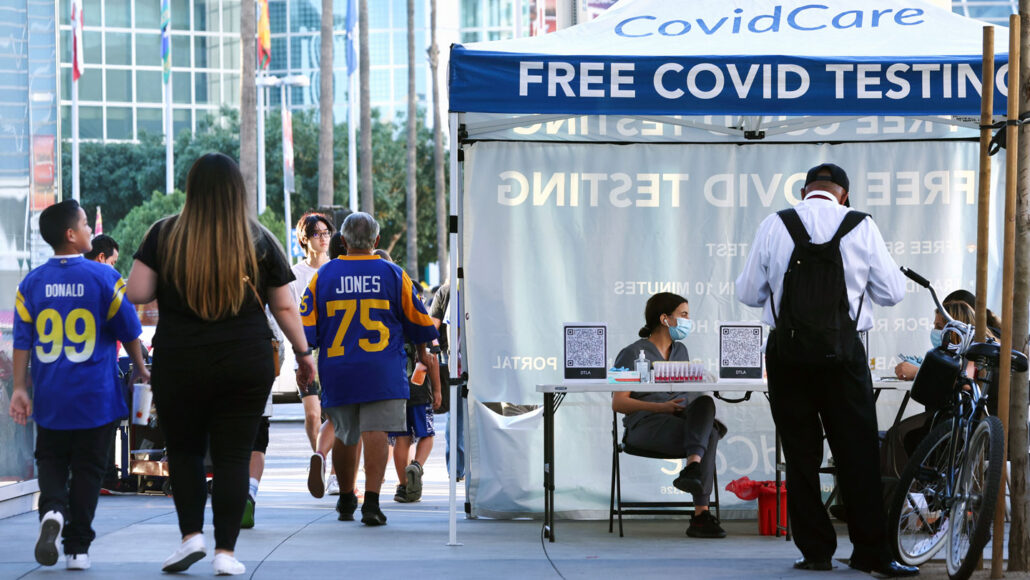 People walking past a COVID testing booth to the 2022 Super Bowl, several wearing Rams jerseys