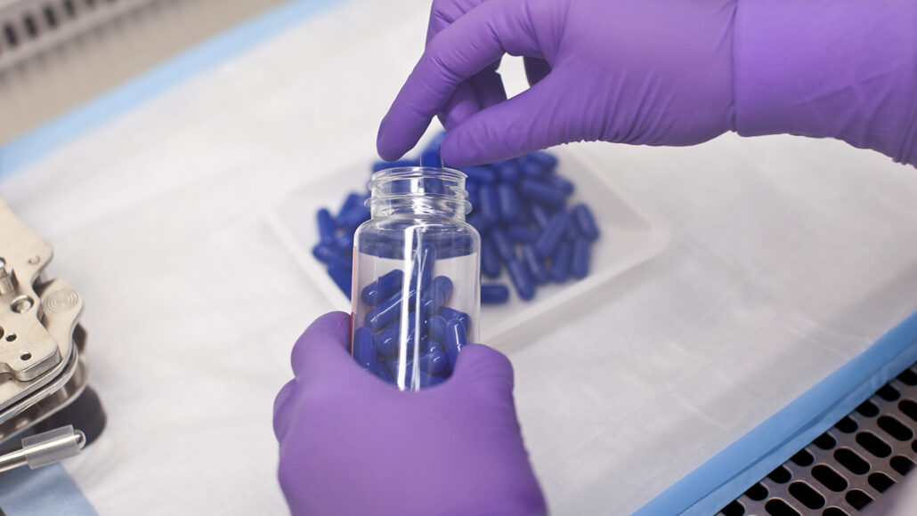 image of purple gloved hands filling a bottle with fecal transplant pills