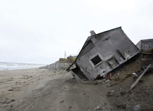 photo of a house falling into the sand on a beach in Shishmaref, Alaska