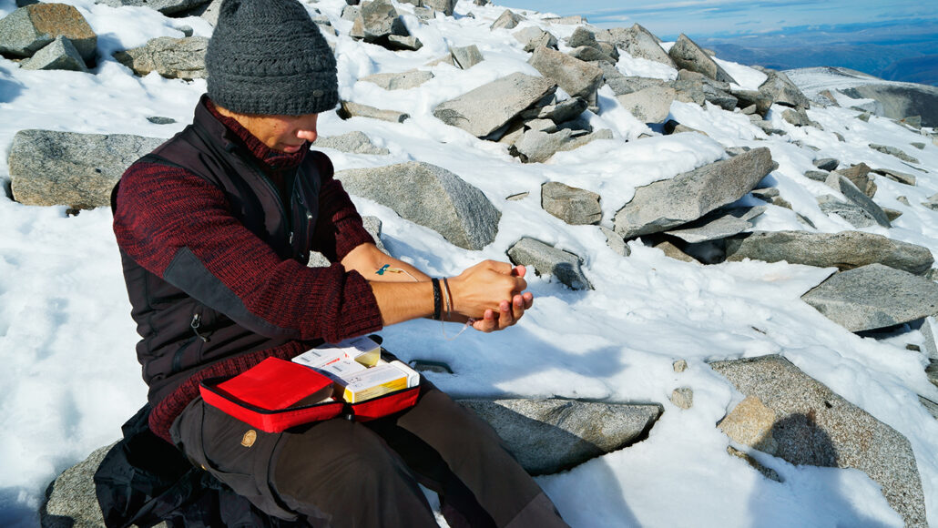A man administering an infusion to treat hemophilia while sitting on a rock in a snowy backdrop