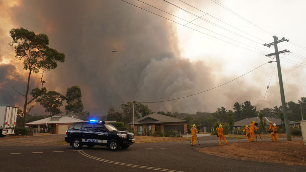 photo of a police car in the foreground with cloud of smoke billowing above Yanderra township buildings