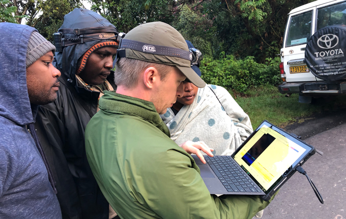 four researchers look at a laptop in the field