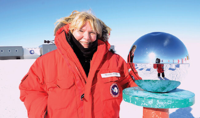 Janet Raloff wearing a red parka and standing next to a reflective sphere in Antarctica