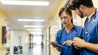 two medical professionals standing in a hallway looking over a chart
