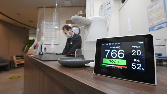 photo of someone behind the front desk of a hotel in Japan with an air quality monitor in the foreground