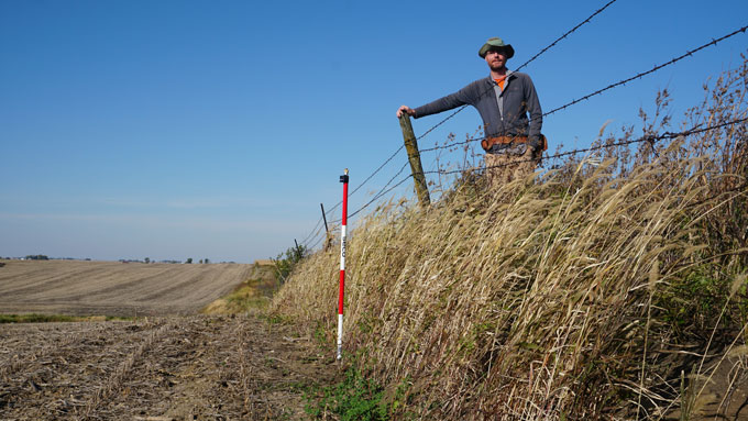 photo of Isaac Larsen standing next to a barbed wire fence on an erosion encampment