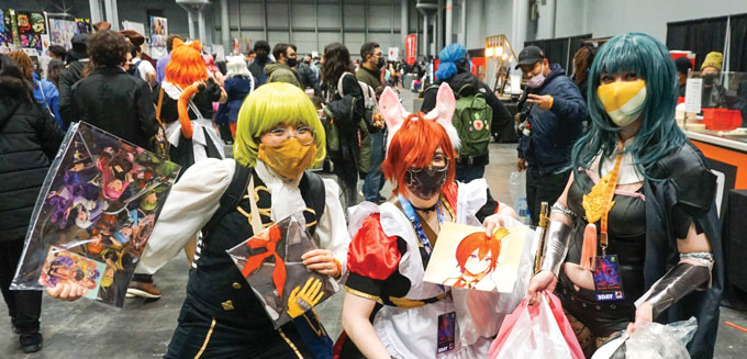 a group of three people wearing wigs and costumes holding artwork with the crowd in the background