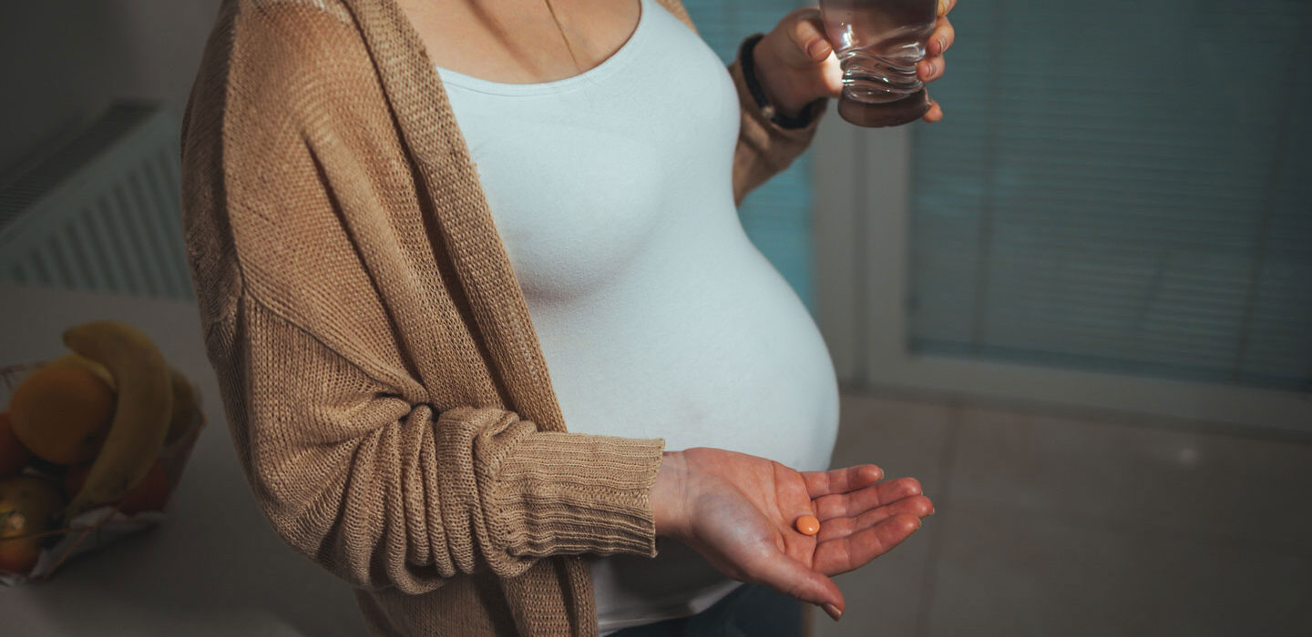 pregnant person holding a pill in one hand and a glass of water in the other hand
