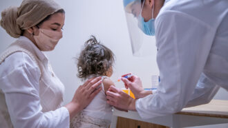 A woman holds a young child as a medical professional gives them a shot