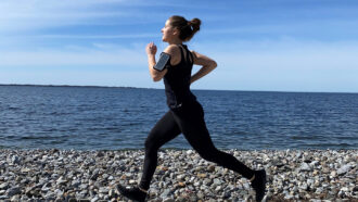a woman running along a rocky shore, with a phone strapped to her arm
