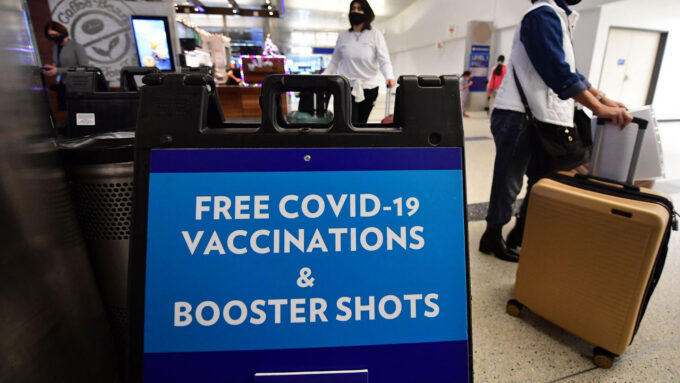 sign that reads "Free COVID-19 Vaccination & Booster Shots" in an airport setting