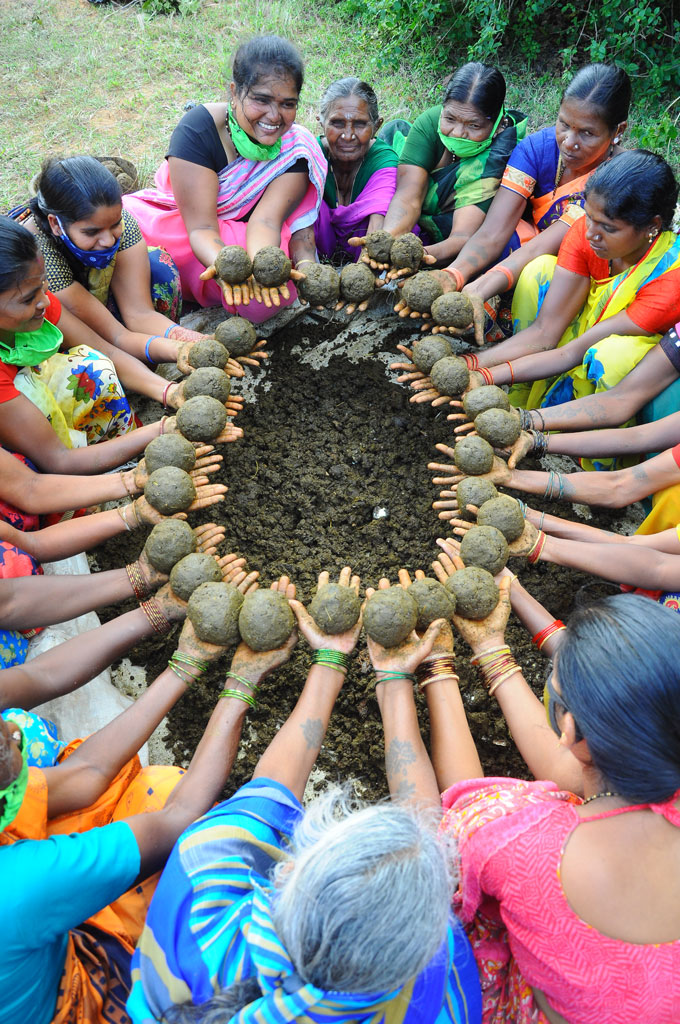 una foto de un círculo de mujeres indias vestidas de colores vivos sosteniendo bolas de fertilizante del tamaño de la palma de la mano