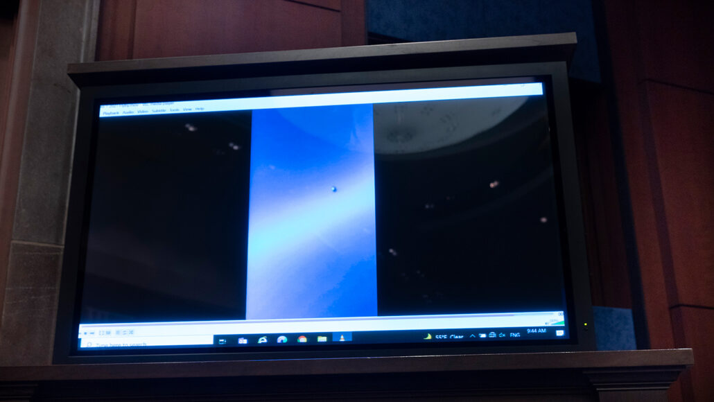 a picture of a large screen showing a video of an unidentified aerial phenomenon during a congressional hearing