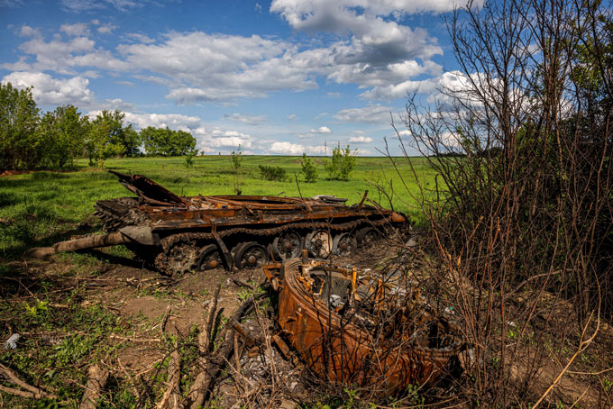 a charred, destroyed tank sits in a field, surrounded by destroyed vegetation