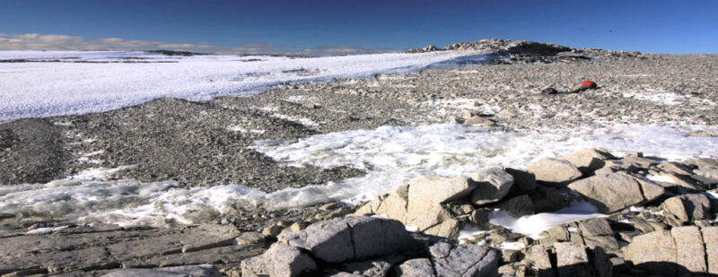 A series of small ridges in the rocky terrain between the foreground boulders and background snow on islands roughly 100 kilometers from Pine Island and Thwaites glaciers in Antarctica.