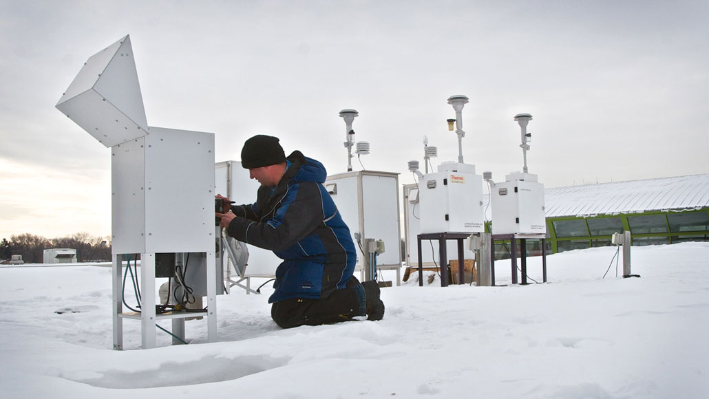 a photo of a man kneeling in the snow to adjust machinery used to monitor air quality