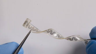 a flexible clear implant with a wavy design in the center, held up by tweezers