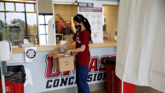 a person collecting COVID-19 swabs into a box at a concession stand with the University of Massachusetts Amherst logo