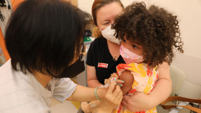 a woman holds a child as a medical professional gives the child a shot
