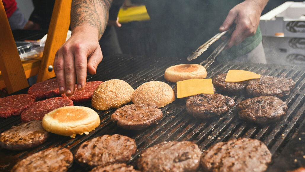 Burger patties in various levels of doneness and buns arranged on a grill