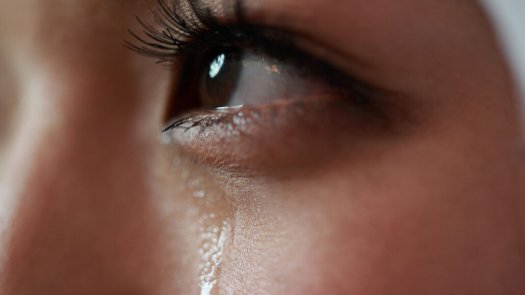 a close-up on a person's eye, with a tear streaming down their cheek