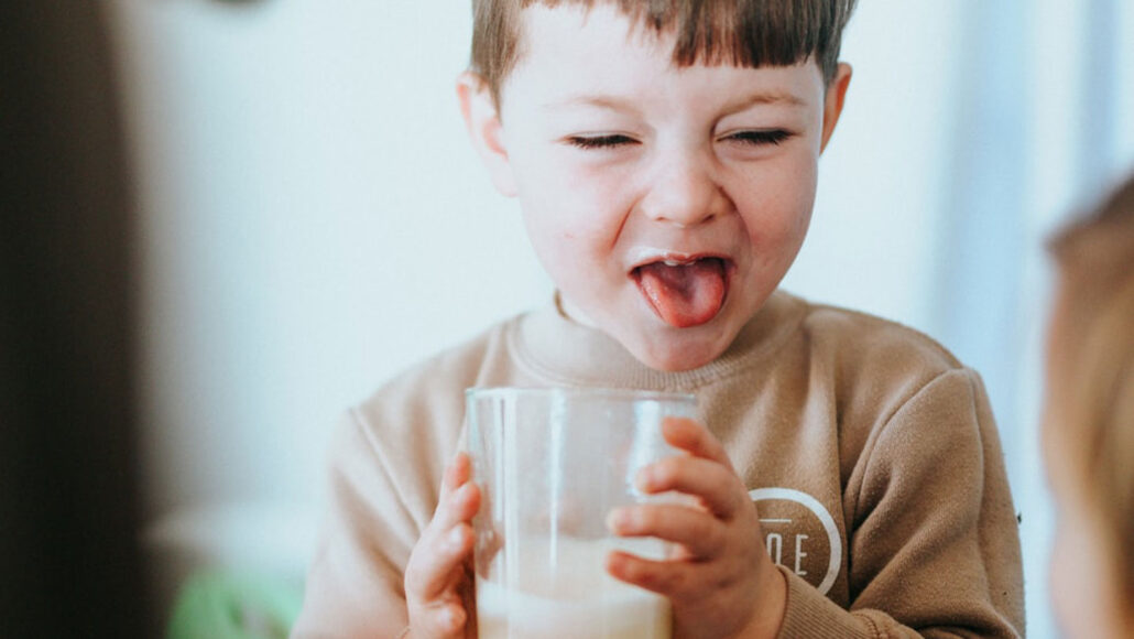 a child holding a glass of milk grimaces