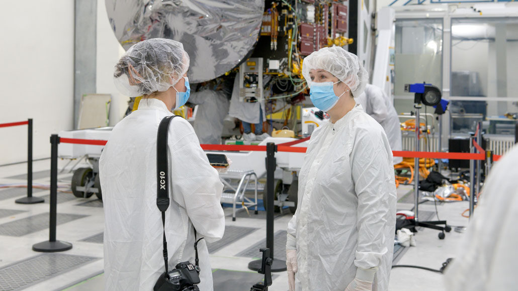 Lindy Elkins-Tanton wears clean room attire and stands in front of the spacecraft for NASA’s Psyche mission