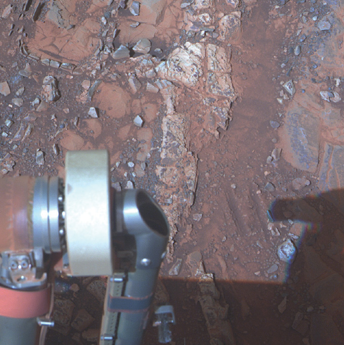 pale rock on the Martian surface with Opportunity's arm in the foreground