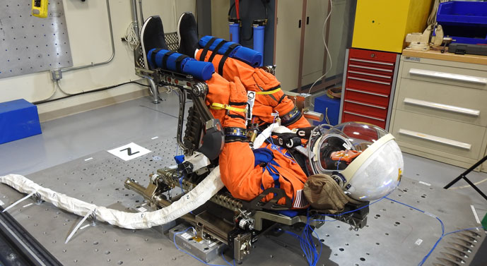 a faux astronaut, wearing orange jumpsuit and helmet lying back in a chair