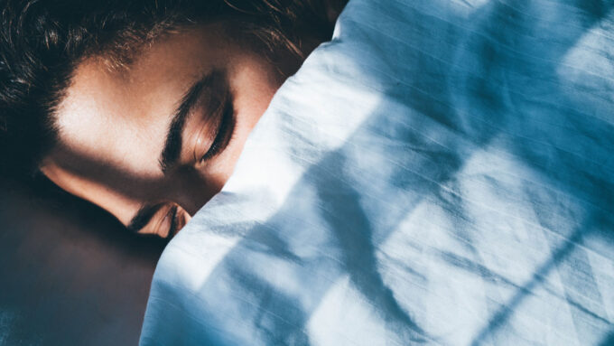 image of the face of someone sleeping in bed under a blue sheet