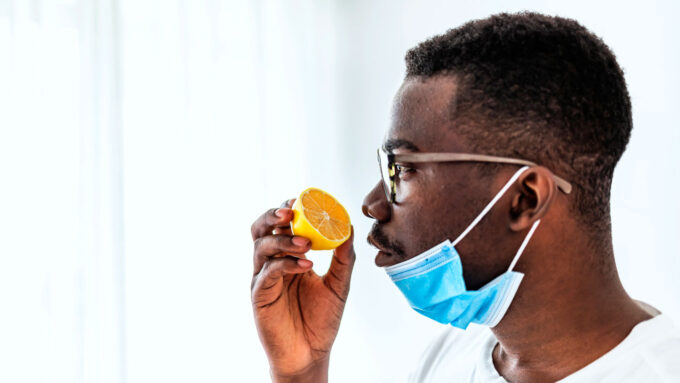 A man has lowered his face mask to smell a sliced lemon.