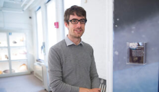 Robin Wordsworth stands in front of a martian meteorite exhibit wearing a gray sweater and glasses