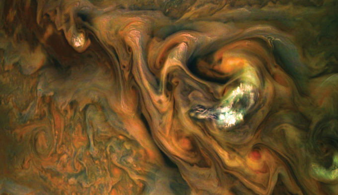 afbeelding van oranje, witte, groene en bruine wolken die wervelen in de atmosfeer van Jupiter