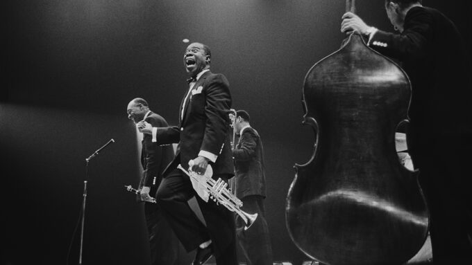 black and white image of Louis Armstrong holding a trumpet surround by other jazz musicians