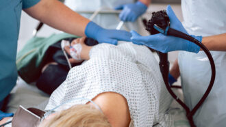 a person lying on a hospital bed with two medical professionals standing over them with various medical equipment