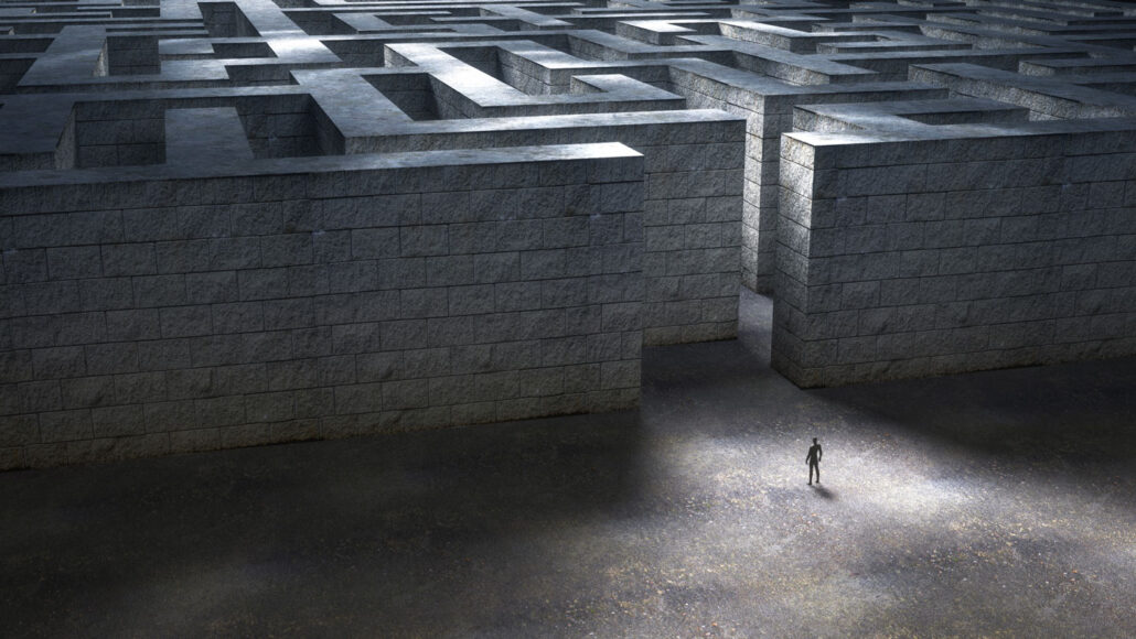 A single person stands in front of an entrance to a maze with tall walls